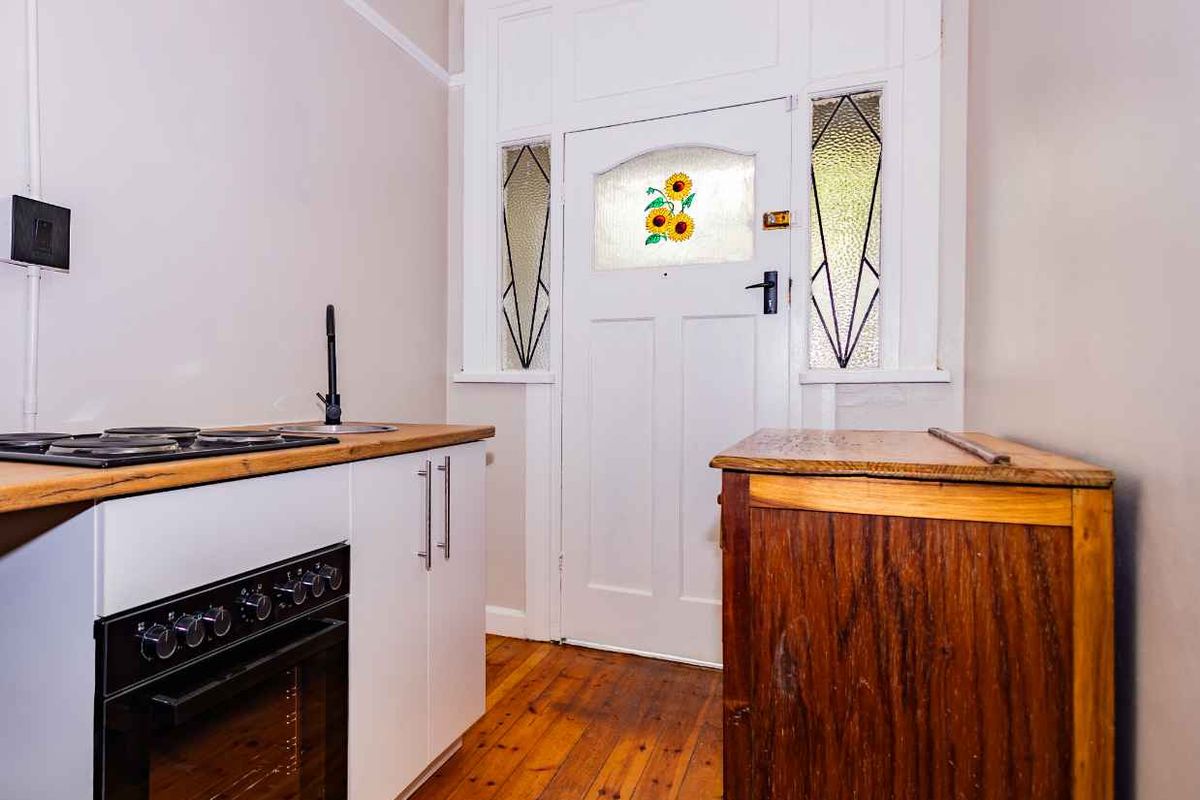 Compact kitchen area featuring a built-in oven, hob, and sink, set against a classic door with decorative leaded glass panels and timber flooring.