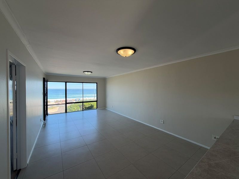 Spacious open-plan living area featuring neutral tiled flooring, large windows with ocean views, and clean finishes, ready for personalization.