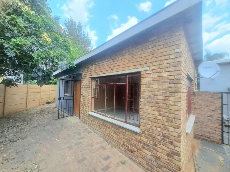 Exterior view of a face brick cottage featuring a paved patio area, metal security gate, and metal-framed windows.