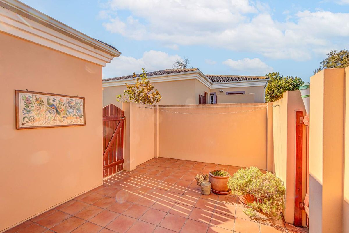 A private, paved courtyard area featuring perimeter boundary walls, a wooden pedestrian gate, and a wall-mounted clothesline.