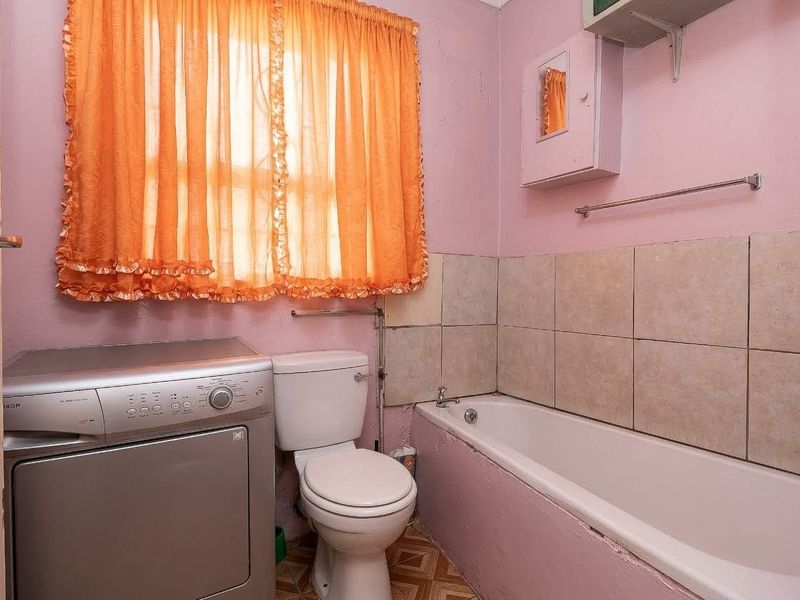 A dated bathroom featuring a standard bathtub, toilet, and tiled splashback, requiring cosmetic updates and repairs to the door frame and wall finishes.