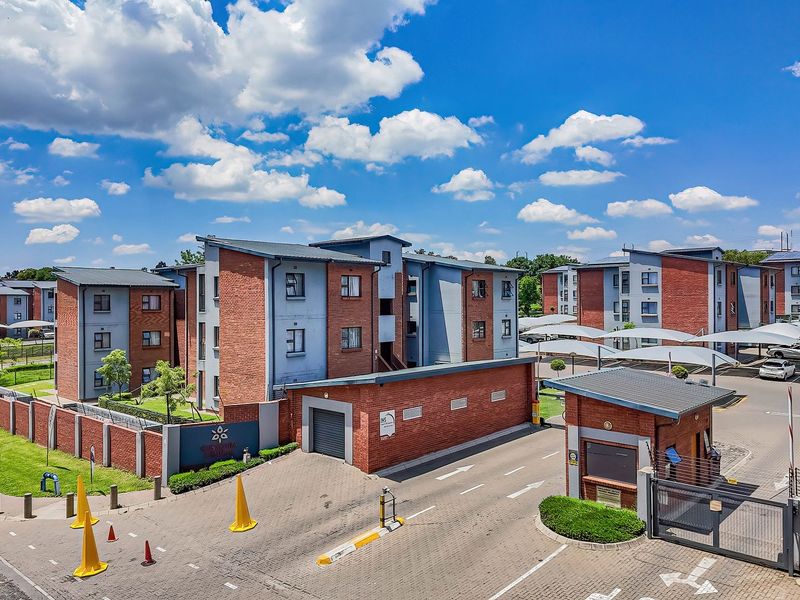 Aerial view of a modern apartment complex featuring brick facades, secure gated entrance, guard house, and covered parking bays.