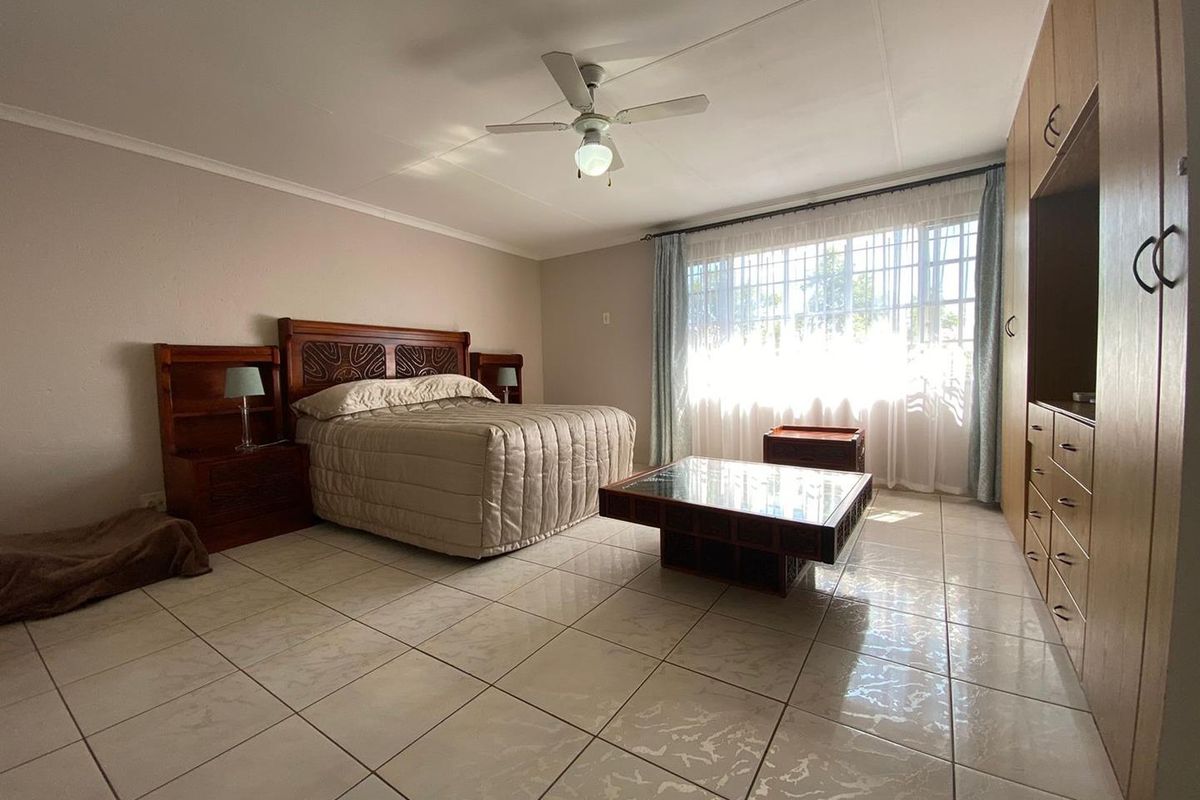 Spacious bedroom featuring large format floor tiles, built-in wooden cabinetry, and a ceiling fan, offering a bright and functional living space.