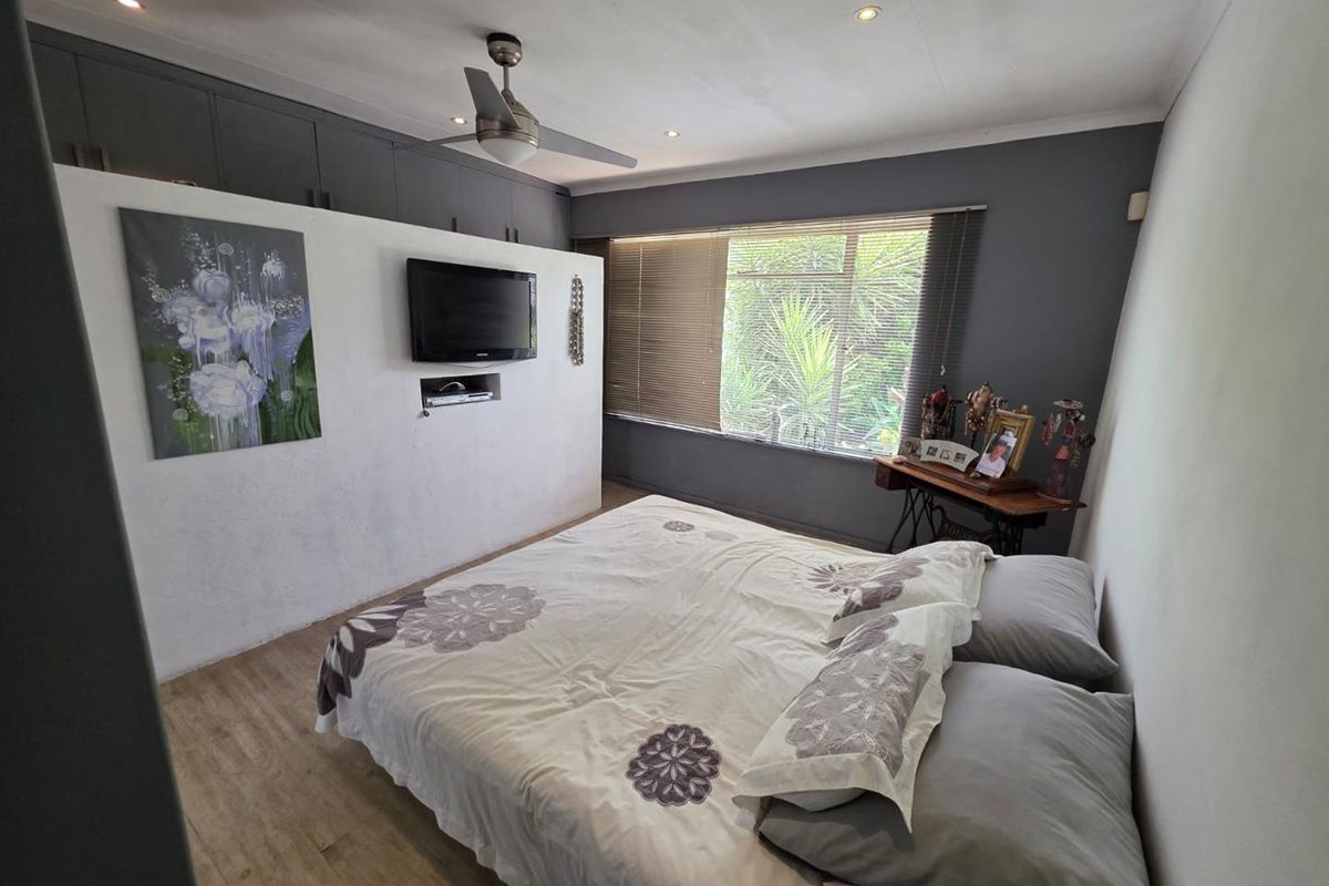 A well-maintained bedroom featuring a built-in partition wall, overhead ceiling fan, recessed lighting, and large windows with venetian blinds.