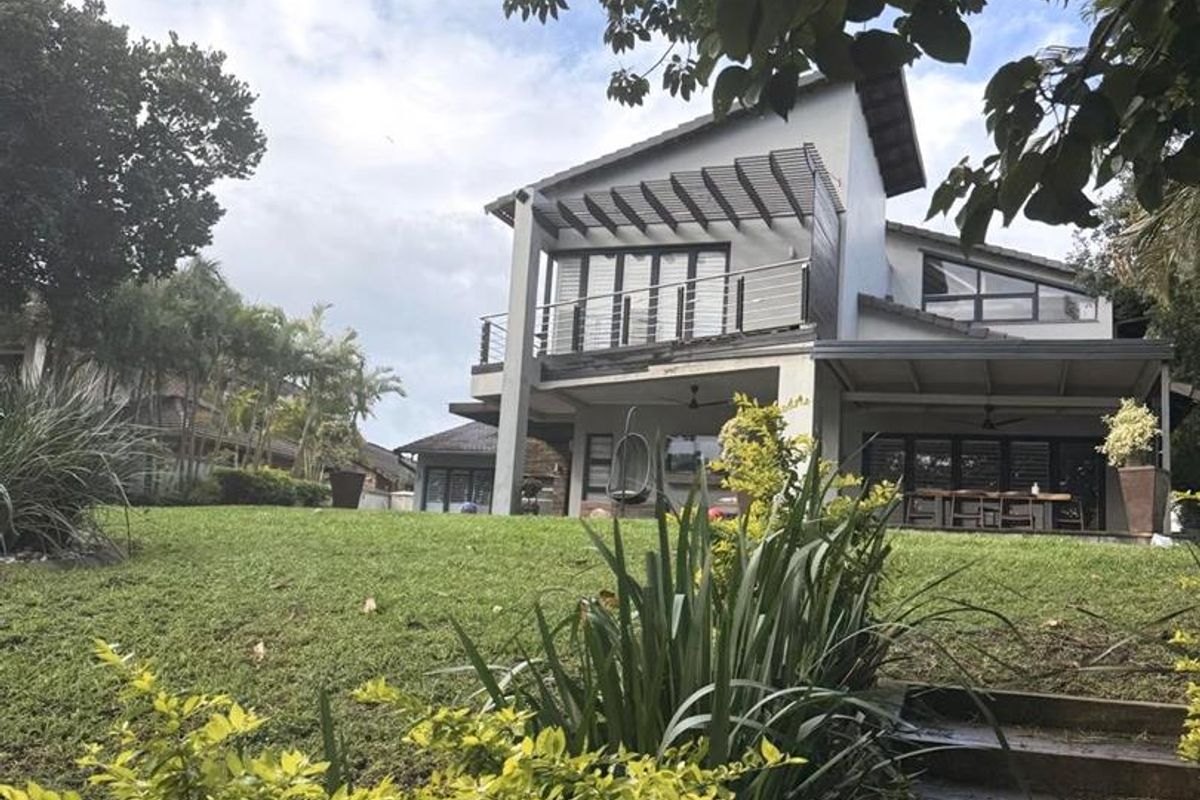 Rear view of the property featuring a landscaped garden, stone steps, and a covered balcony with a pergola structure.
