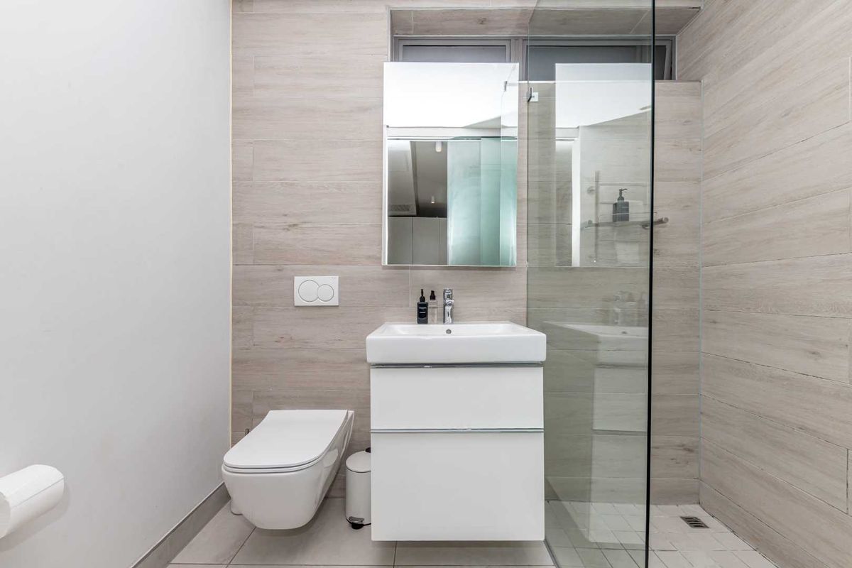 Modern bathroom featuring a wall-hung toilet, sleek vanity cabinet with basin, and a glass-enclosed shower with neutral wood-look wall tiling.