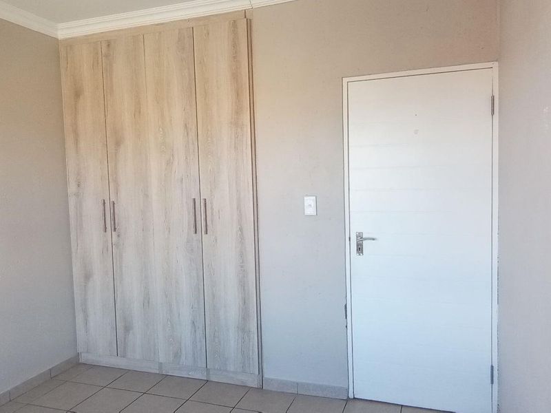 A clean, empty bedroom featuring neutral walls, tiled flooring, and modern light wood-finish built-in cupboards.