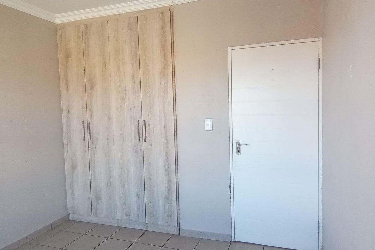 A clean, empty bedroom featuring neutral walls, tiled flooring, and modern light wood-finish built-in cupboards.