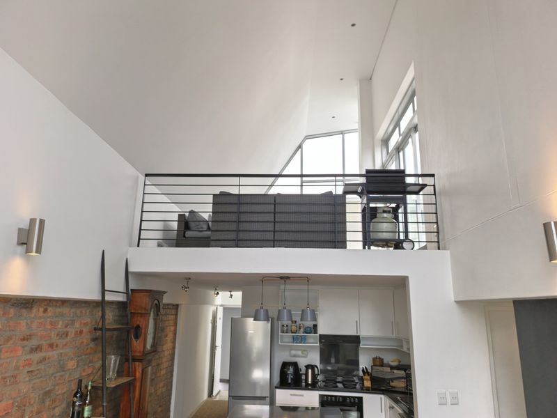 Modern open-plan apartment featuring a double-volume living space with a mezzanine level, exposed brick accents, and a contemporary kitchen with integrated appliances.