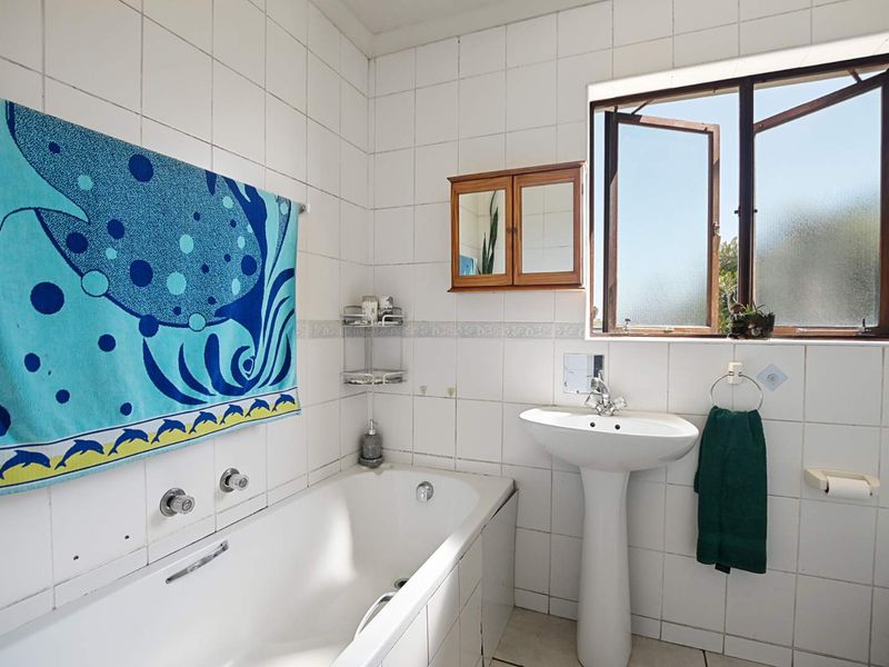 A functional bathroom featuring a pedestal basin, built-in bathtub, and tiled walls, with natural light provided by a side-opening casement window.