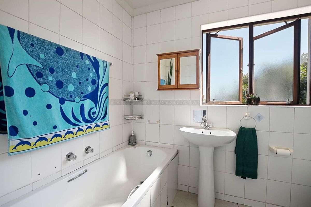 A functional bathroom featuring a pedestal basin, built-in bathtub, and tiled walls, with natural light provided by a side-opening casement window.