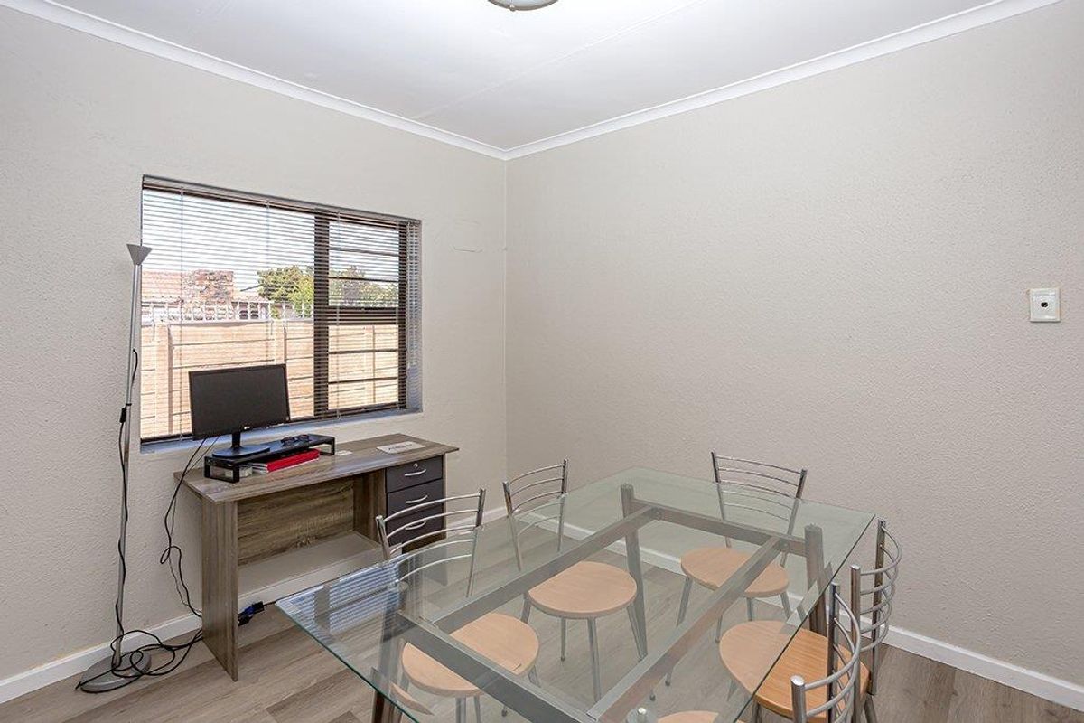 A well-maintained bedroom featuring neutral wall tones, laminate flooring, and an aluminium-framed window with fitted blinds.