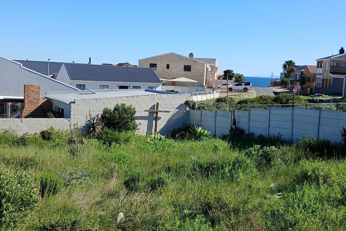A vacant residential plot featuring overgrown vegetation, enclosed by a precast concrete boundary wall with electric fencing, situated in a coastal neighborhood.