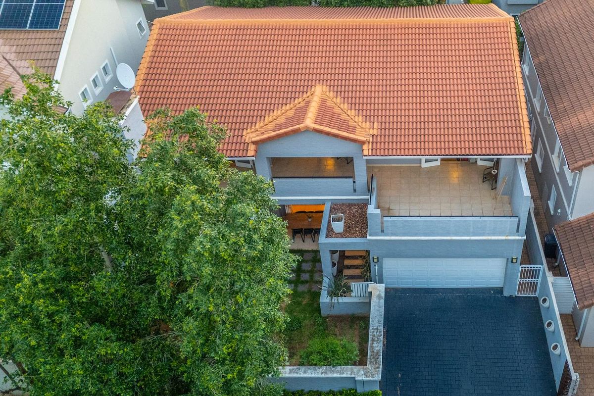 Aerial view of a residential property featuring a terracotta tiled roof, solar panels, a double garage, and a paved driveway.