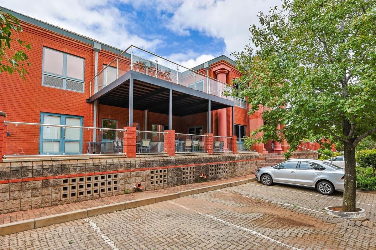 Exterior view of a commercial building featuring a raised patio with glass balustrades, brick facade, and paved parking area.