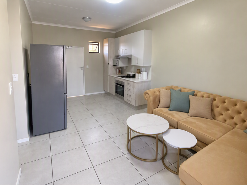 An open-plan living area featuring a modern kitchen with built-in cabinetry, oven, and hob, seamlessly integrated with the living space and tiled flooring.
