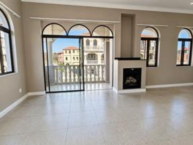 Spacious living area featuring tiled floors, a built-in fireplace, and large arched windows with direct access to a private balcony.