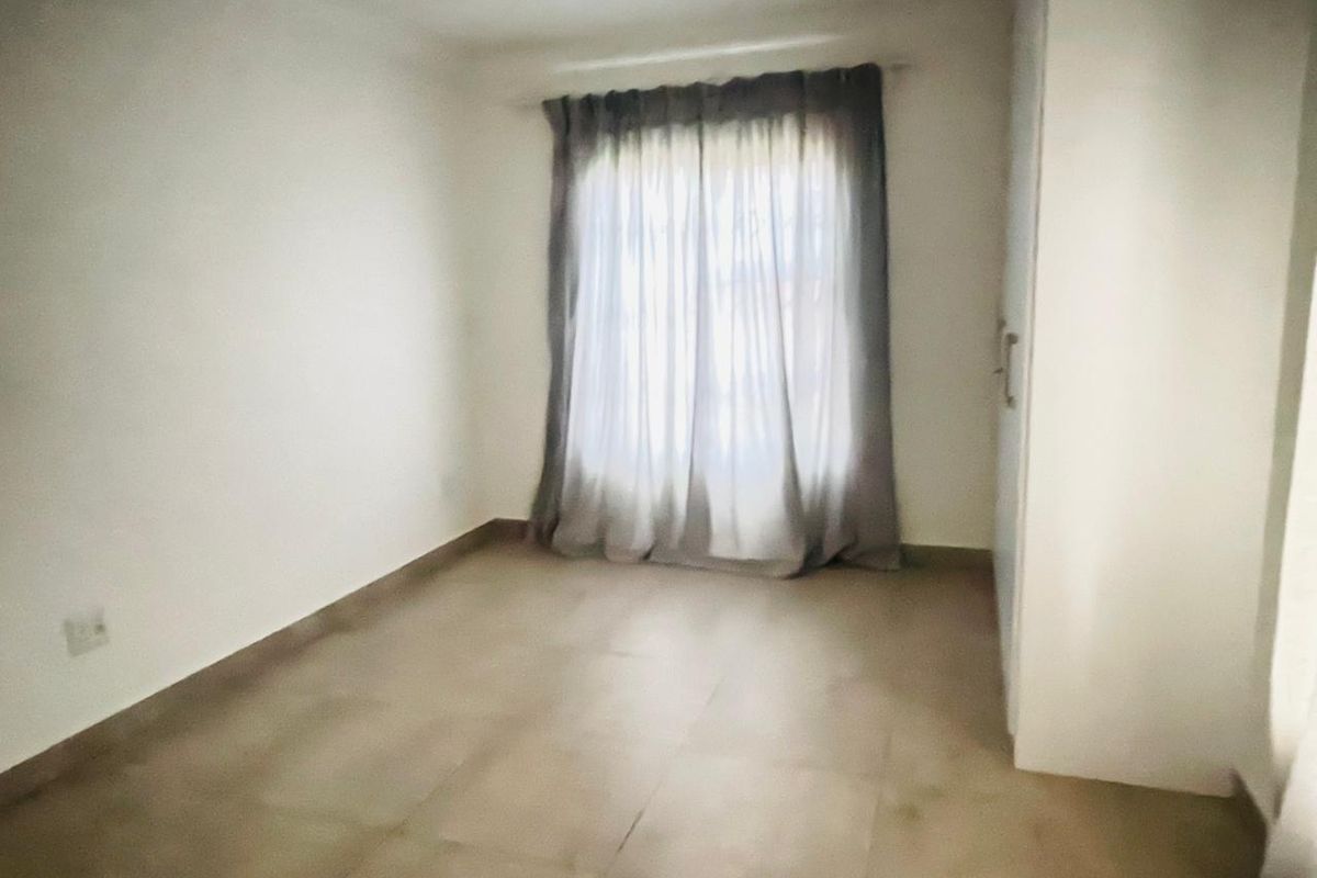A bright, empty bedroom featuring neutral tiled flooring and a built-in wardrobe, offering a clean and versatile space ready for personalization.