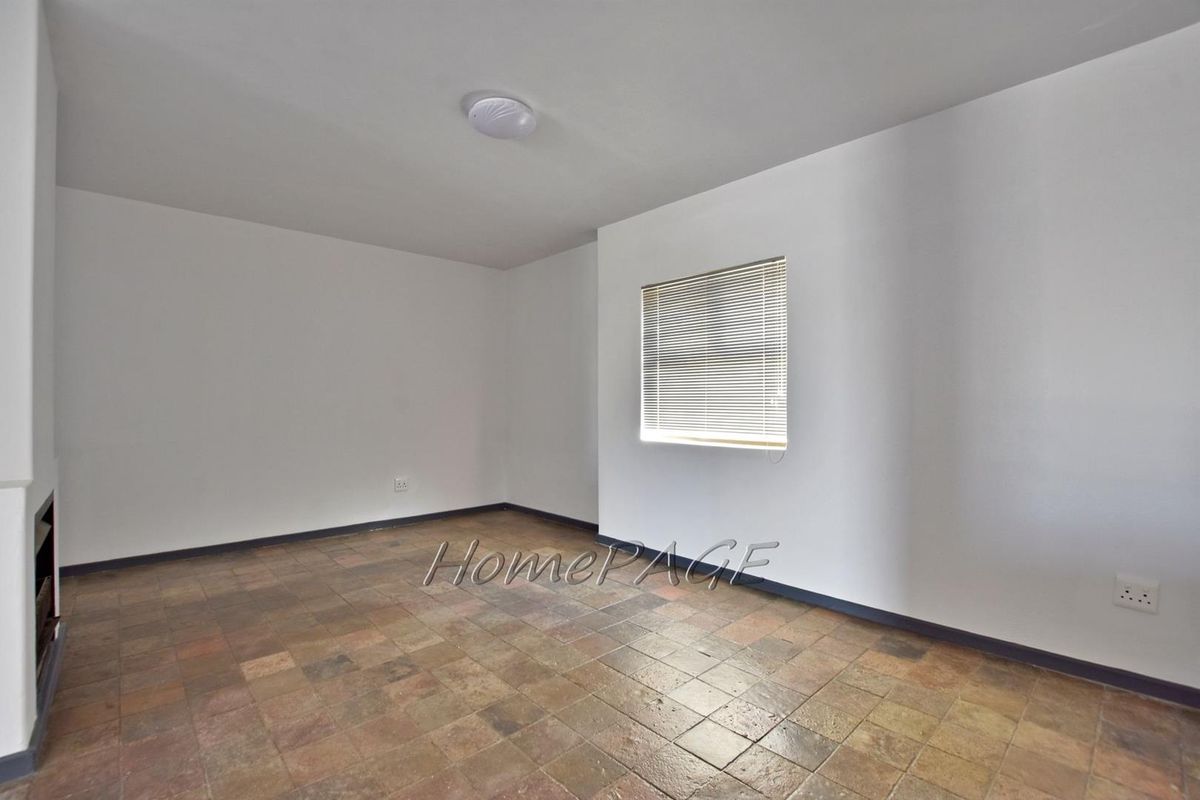 A clean, empty bedroom featuring tiled flooring, a window with fitted venetian blinds, and neutral wall finishes, ready for personalization.
