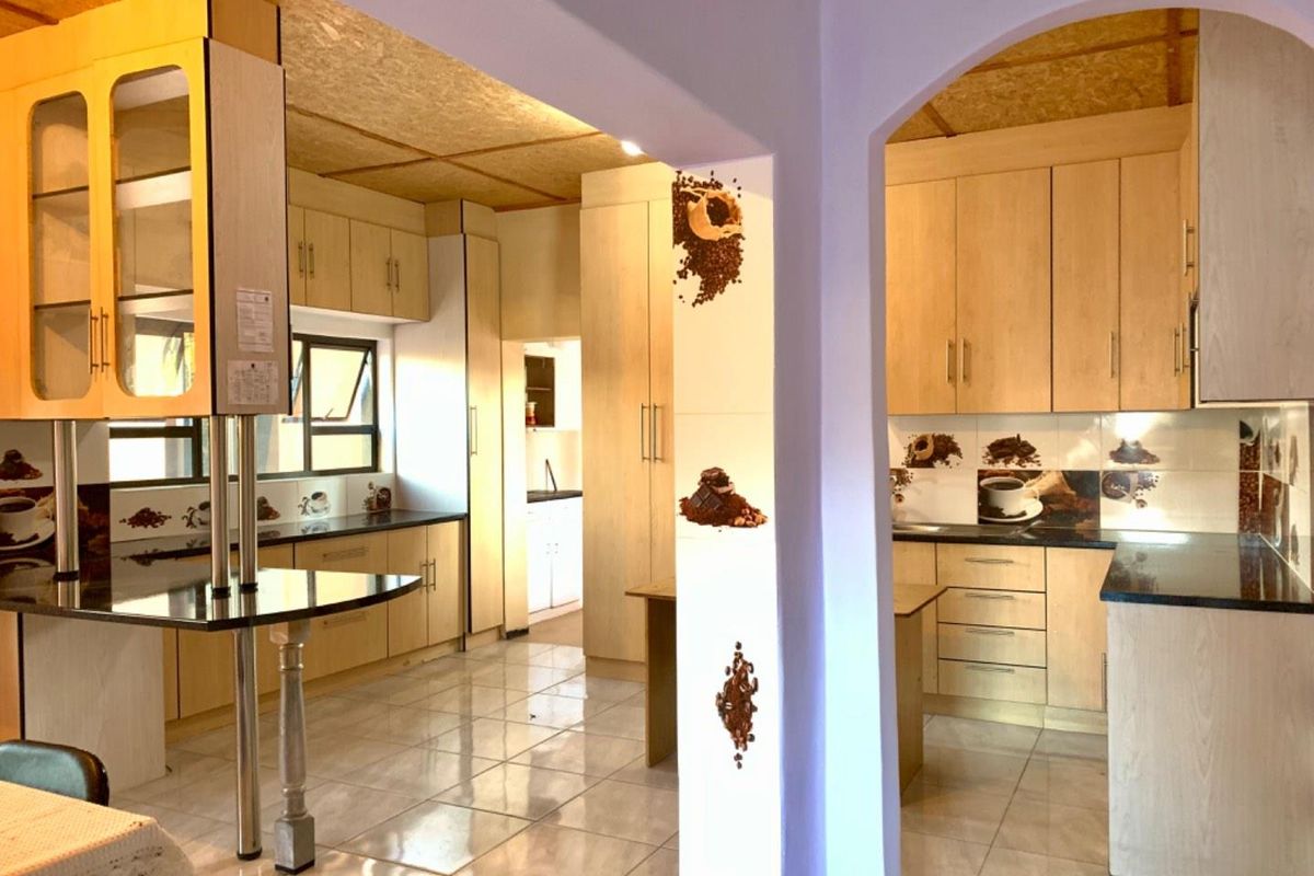 Spacious kitchen featuring light wood cabinetry, dark granite countertops, tiled flooring, and a breakfast bar, with an adjacent scullery area.