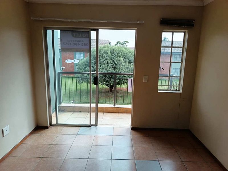 An empty living area featuring tiled flooring, a sliding glass door leading to a balcony, and a window providing natural light.