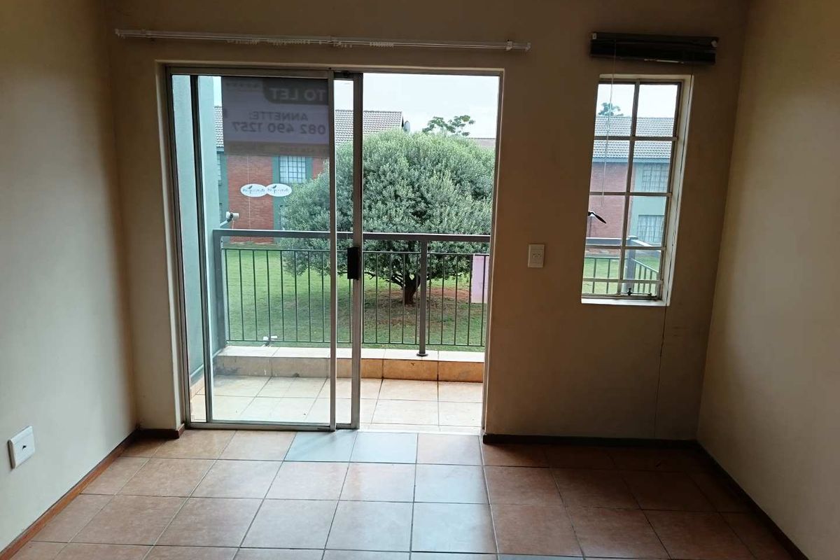 An empty living area featuring tiled flooring, a sliding glass door leading to a balcony, and a window providing natural light.