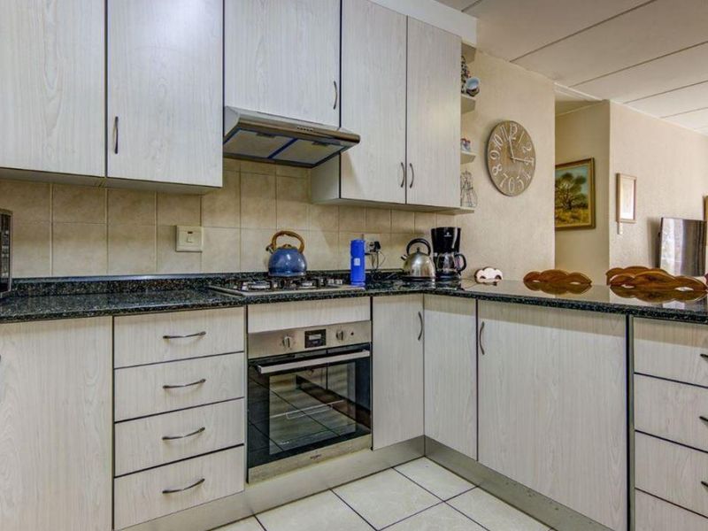 A functional kitchen featuring light wood-grain cabinetry, dark granite countertops, built-in oven, gas hob, and tiled flooring, offering a practical layout for daily cooking.