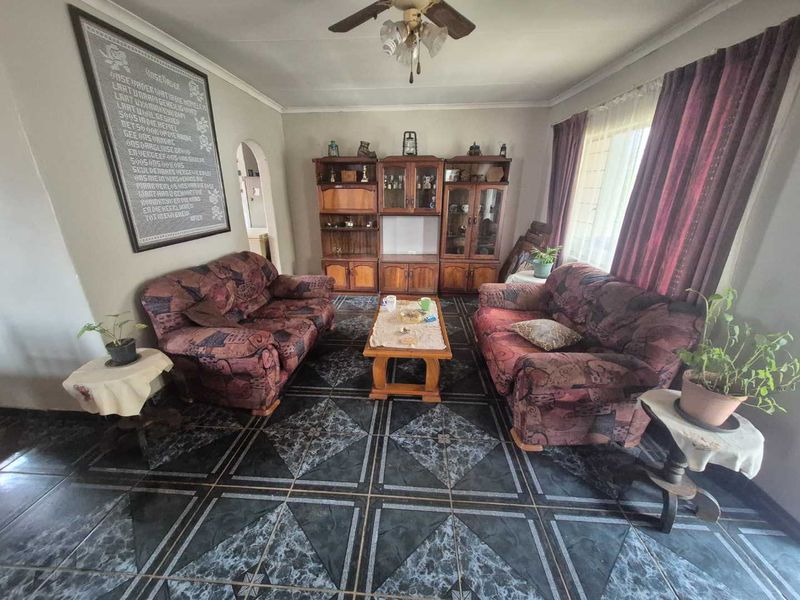 A living room featuring tiled flooring, a ceiling fan, and an arched entryway, offering a functional space with potential for modern updates.