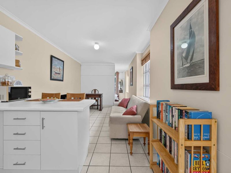 An open-plan living and kitchen area featuring tiled flooring, built-in cabinetry, and security bars on the windows.