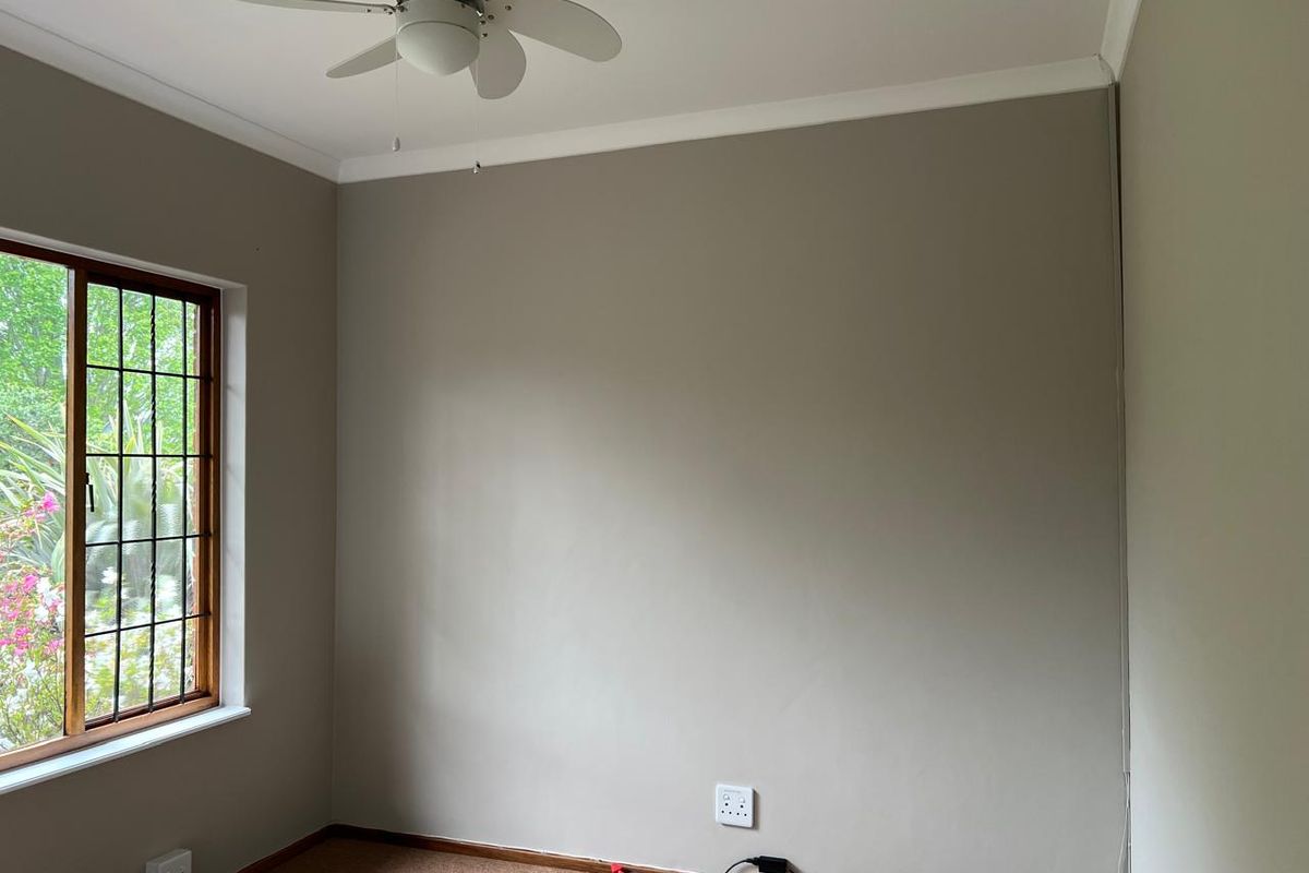 A clean, empty bedroom featuring neutral wall tones, a ceiling fan, and a timber-framed window with security bars.