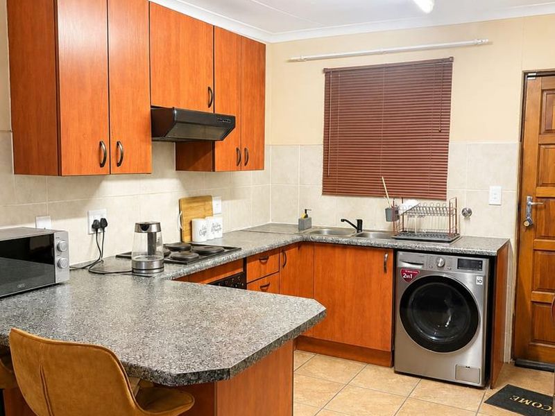 A functional kitchen featuring wood-finish cabinetry, granite-look countertops, tiled flooring, and integrated space for a washing machine.