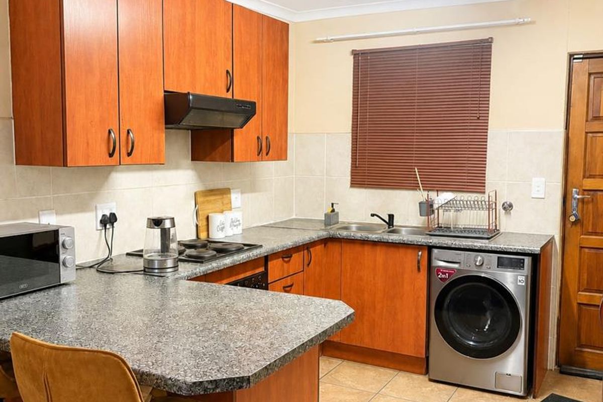 A functional kitchen featuring wood-finish cabinetry, granite-look countertops, tiled flooring, and integrated space for a washing machine.