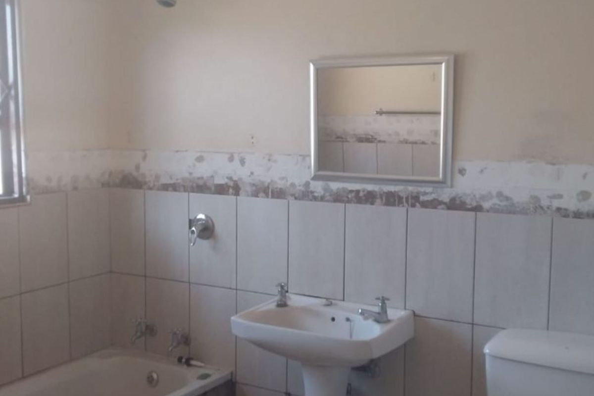 A functional bathroom featuring a bathtub, pedestal basin, and toilet, currently requiring cosmetic repairs to the wall tiling and plaster finish.