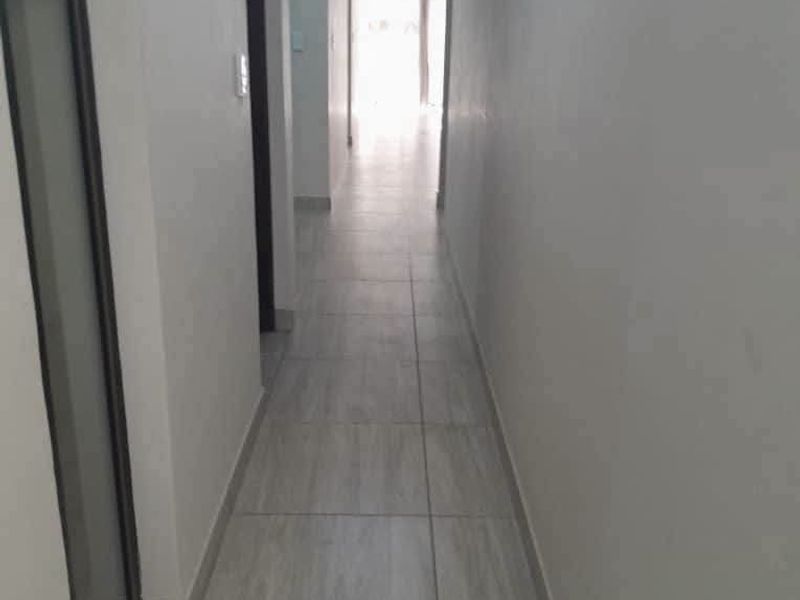 A clean, neutral hallway featuring light-toned tiled flooring and recessed lighting, providing a bright and functional transition space between rooms.