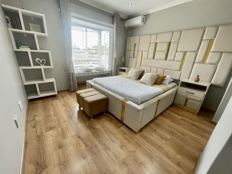 A well-maintained bedroom featuring laminate flooring, a built-in window seat, recessed lighting, and a wall-mounted split-system air conditioner.