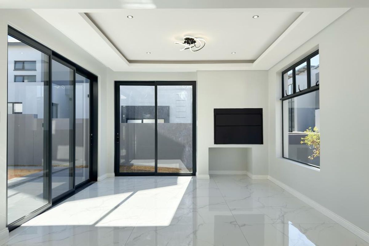 Bright and modern living area featuring large sliding glass doors, marble-look tiled flooring, recessed tray ceiling, and a built-in fireplace.
