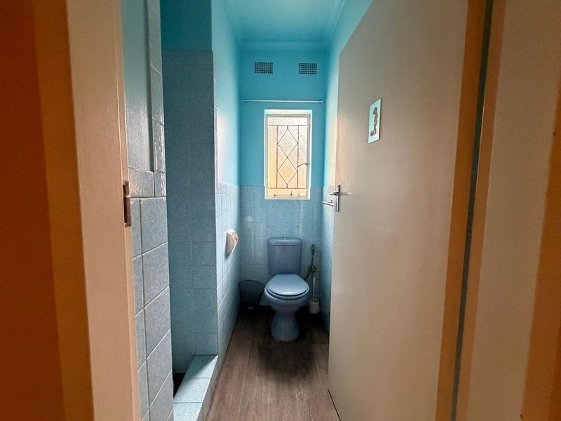 A compact, dated bathroom featuring blue wall tiles, a matching blue toilet, and a leaded glass window.