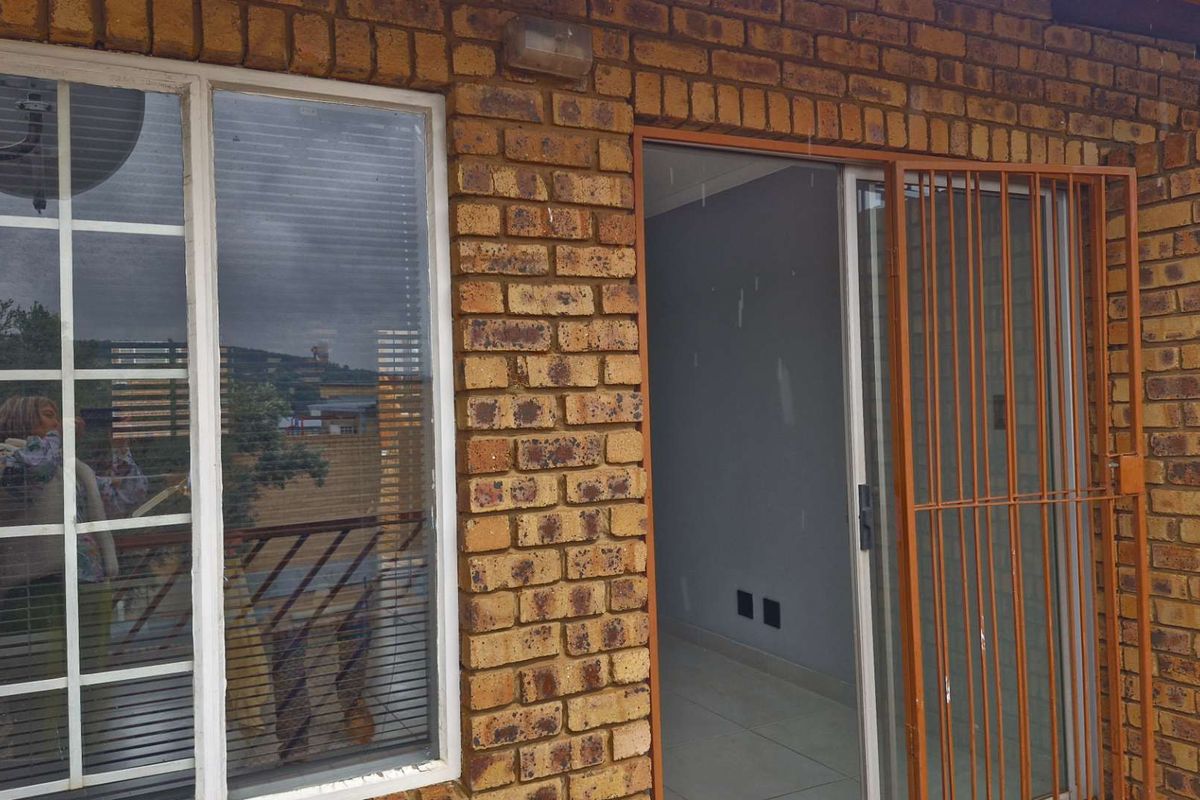 Exterior view of a face brick apartment facade featuring a sliding glass door with a security gate and an aluminium framed window.