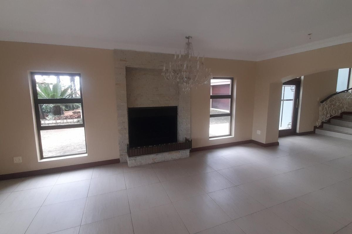 Spacious living area featuring a stone-clad fireplace, tiled flooring, and a decorative chandelier, with an adjacent staircase visible in the background.