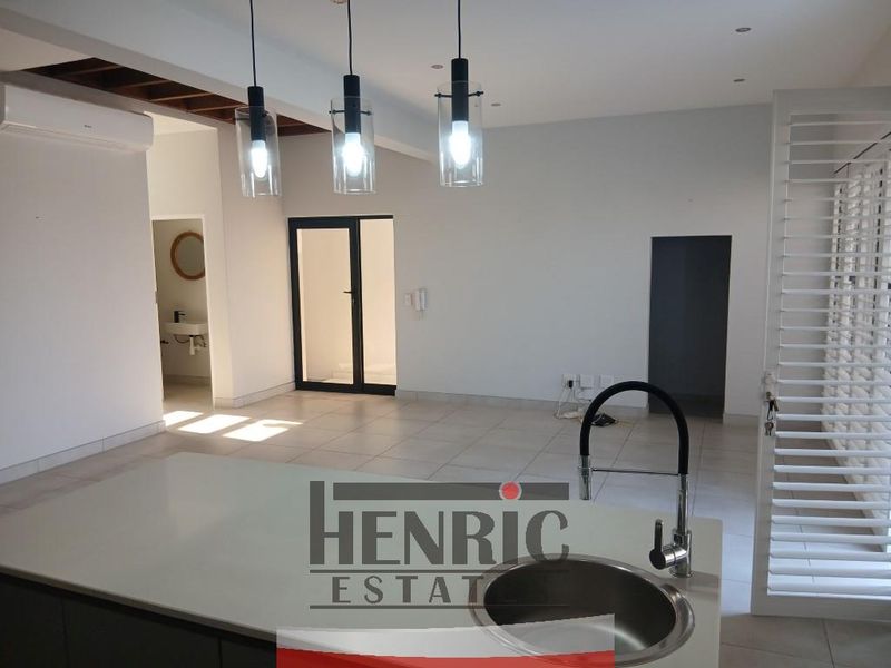Spacious open-plan living area featuring a modern kitchen island with sink, tiled flooring, pendant lighting, and shutter blinds, offering a bright and versatile layout.