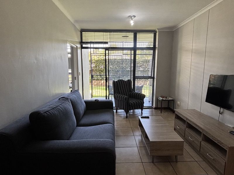 A functional living room featuring tiled flooring, neutral walls, and a large sliding glass door with security gate providing access to the outdoor area.