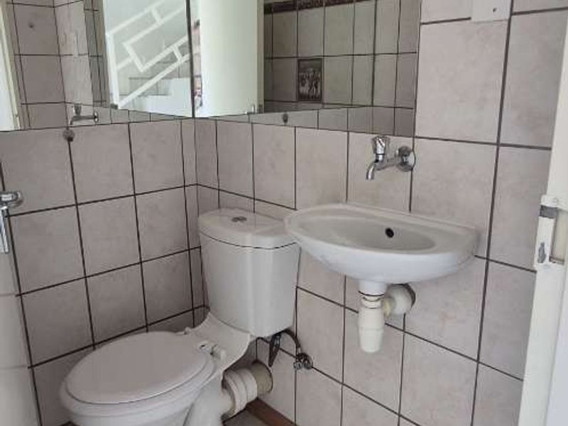 A compact guest bathroom featuring a wall-mounted basin, toilet, and full-width wall mirror with neutral tiled finishes.