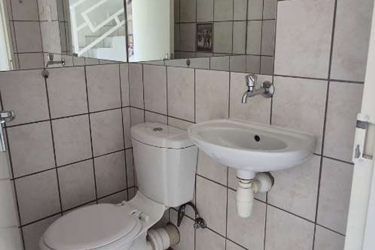 A compact guest bathroom featuring a wall-mounted basin, toilet, and full-width wall mirror with neutral tiled finishes.