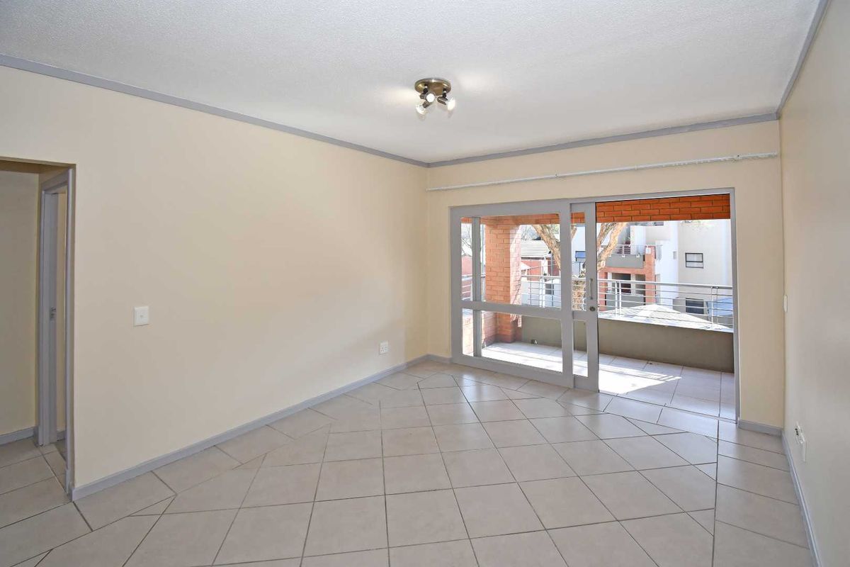 An empty living room featuring neutral tiled flooring and a large sliding glass door providing access to an outdoor balcony area.