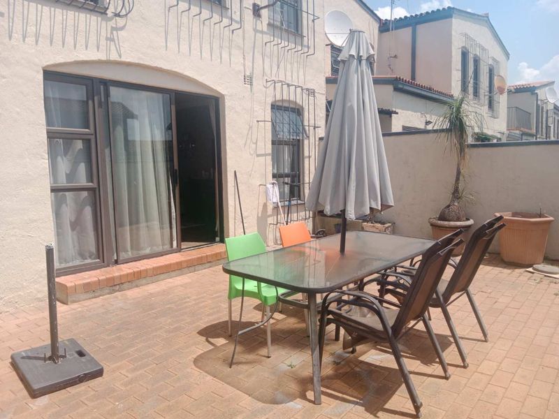 Rear exterior view of a townhouse featuring a brick-paved patio area with a sliding glass door entrance and secure boundary wall.