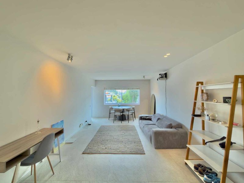 A bright and spacious open-plan living area featuring neutral tiled flooring, recessed lighting, and a large window providing natural light.