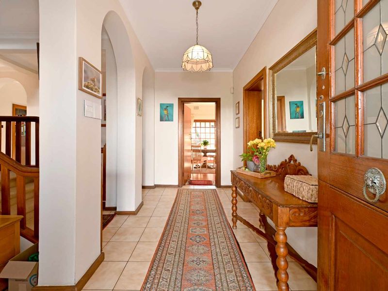 A welcoming entrance hallway featuring tiled flooring, arched architectural details, a timber staircase, and a classic leaded glass timber front door.