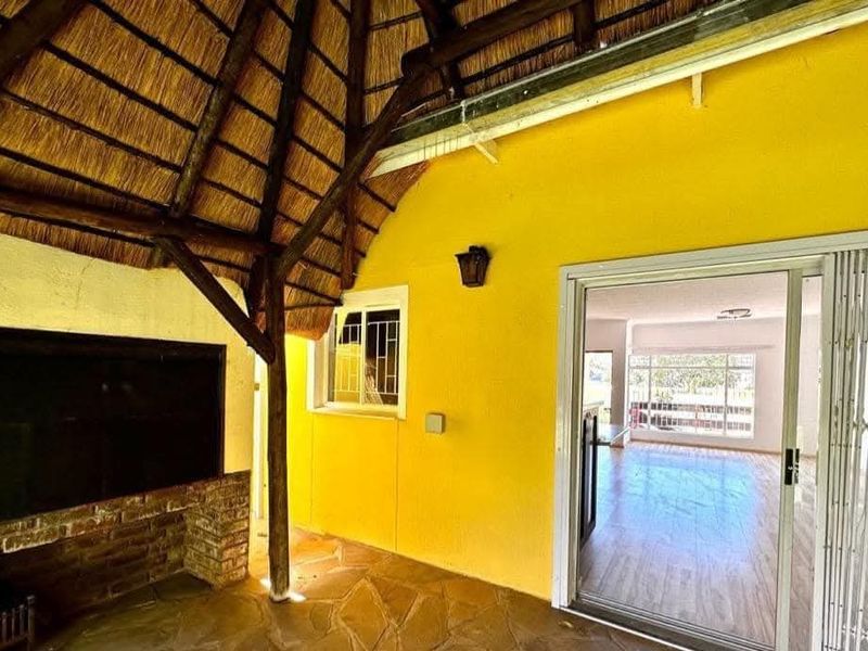 Covered patio area featuring a traditional thatched roof, built-in braai, and stone flooring, providing direct access to the interior living space.