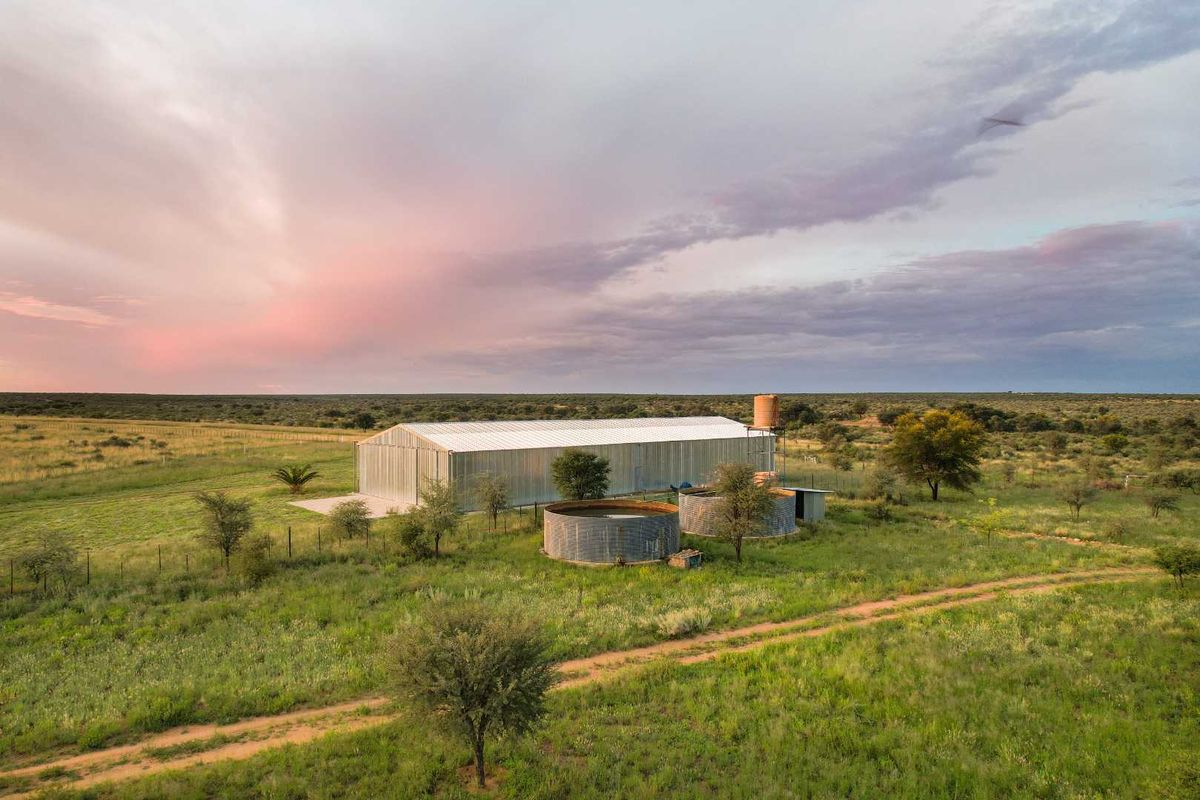 Aerial view of a large metal farm shed with adjacent circular water storage tanks set within a vast rural landscape.
