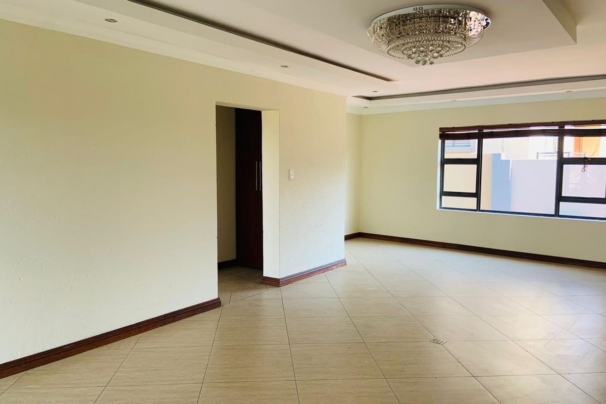 Spacious, light-filled living area featuring tiled flooring, a modern recessed ceiling with a crystal chandelier, and large windows.